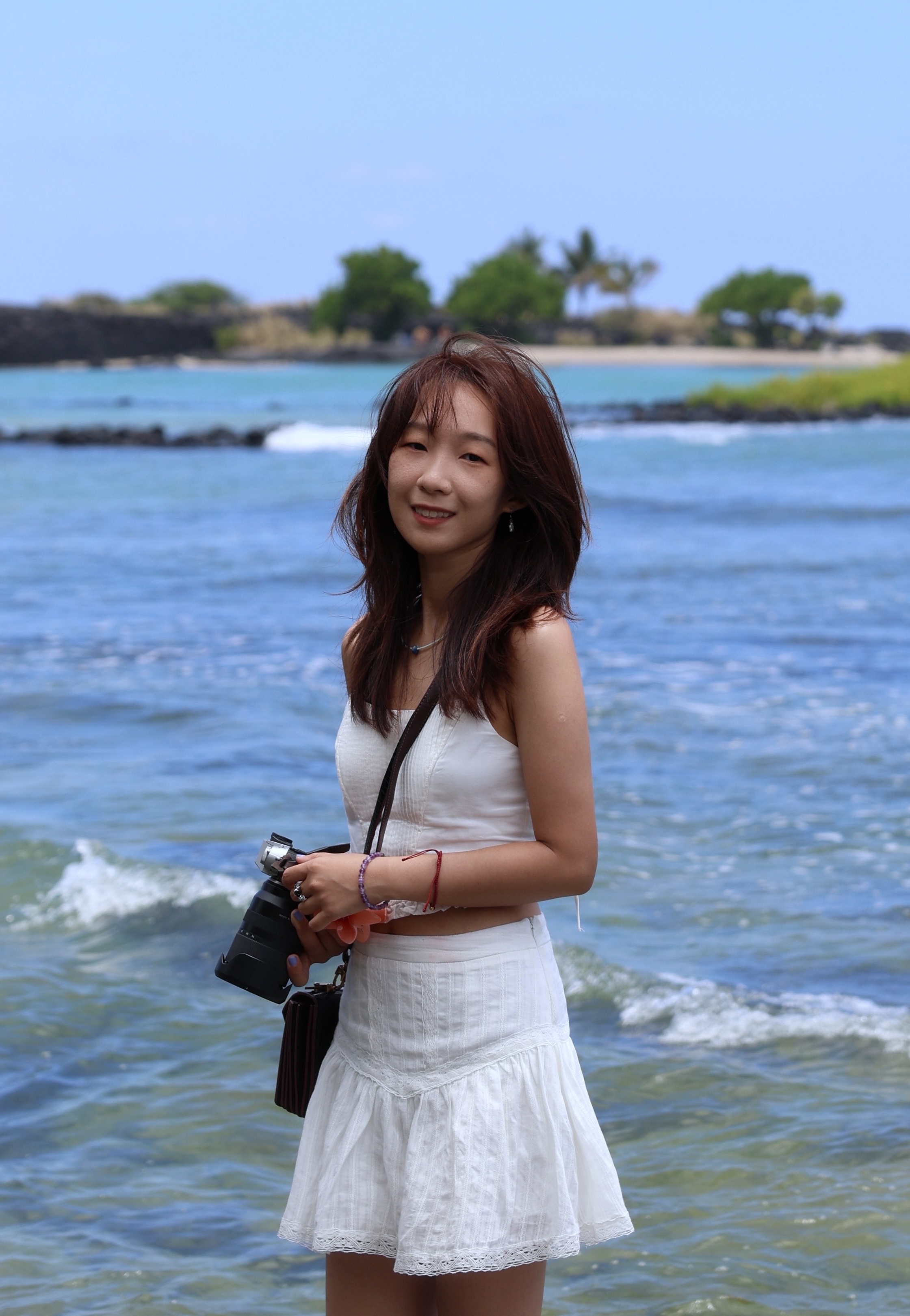 Xinchang standing by the ocean with a camera